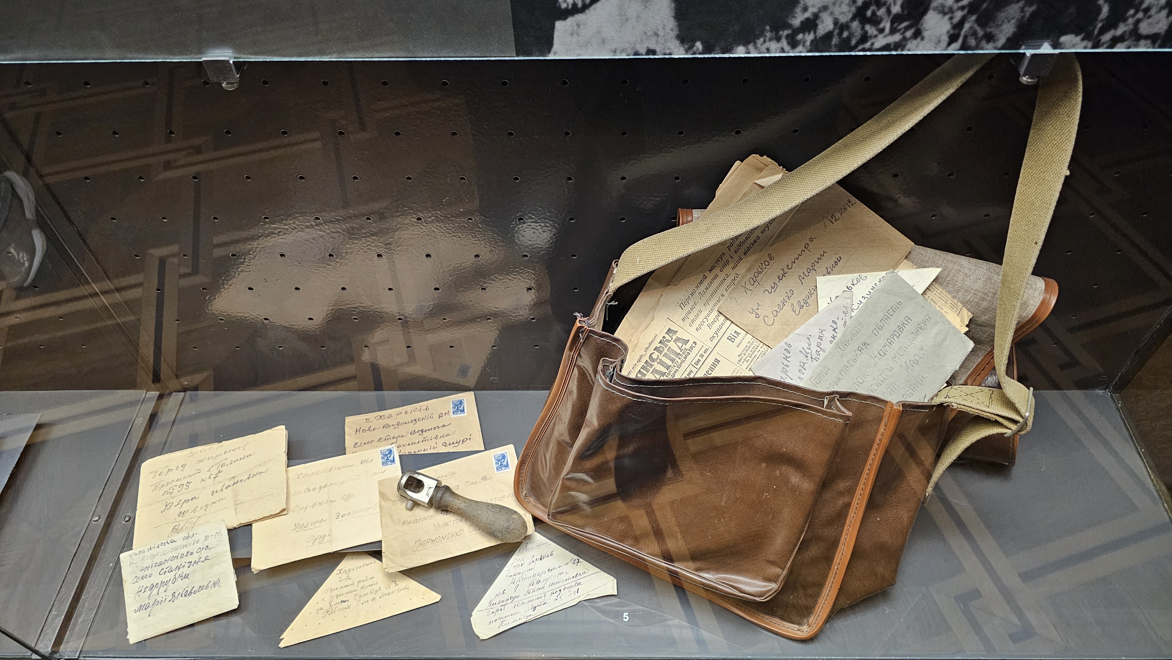Postman's brown leatherbag with a bunch of letters displayed within and outside of it. Envelopes are stamped and handwritten.