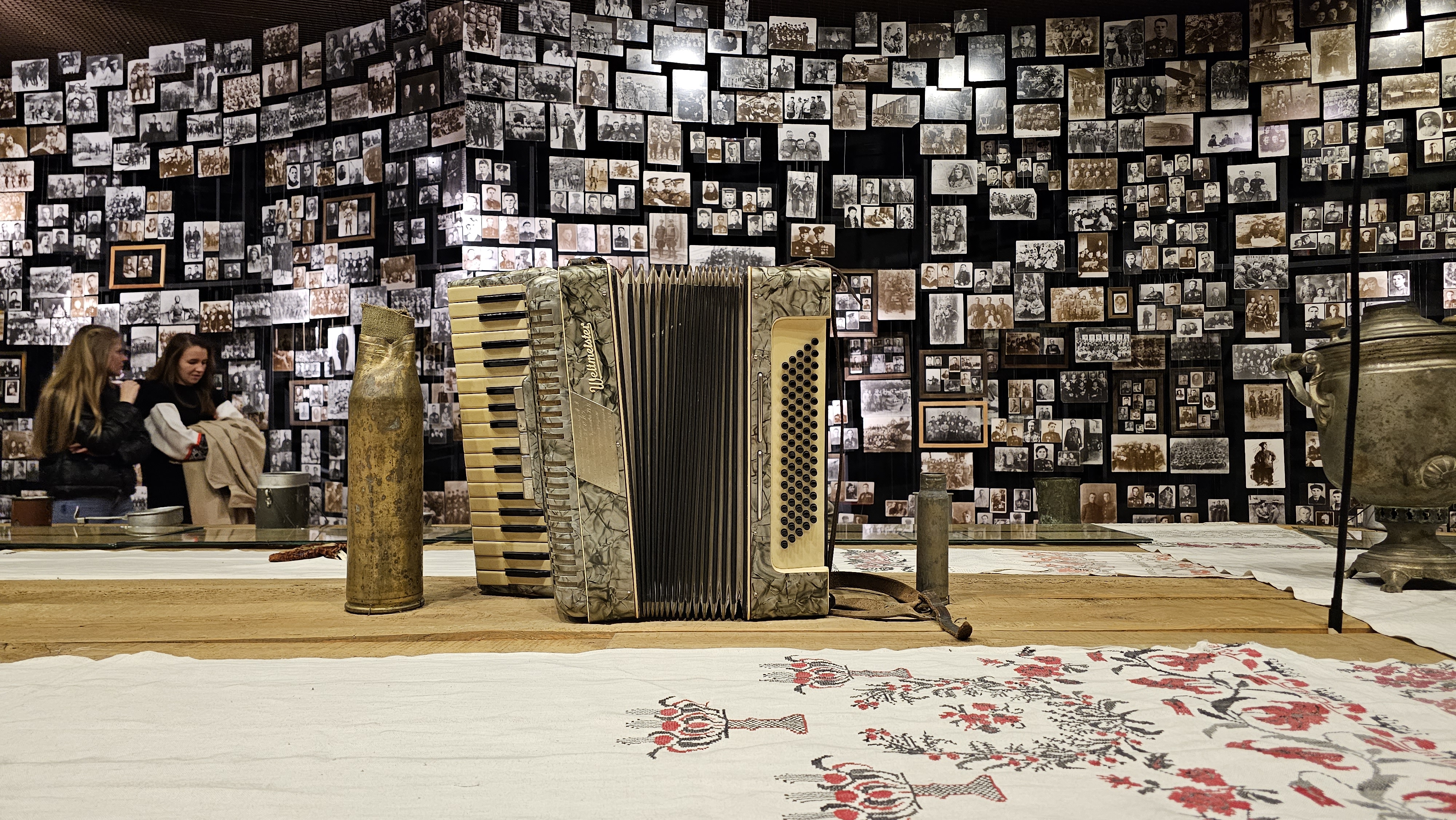 An accordeon is on display on a banquet table covered with traditional tablecloths with Ukrainian embrodery and soldier's mess tins and bottles.