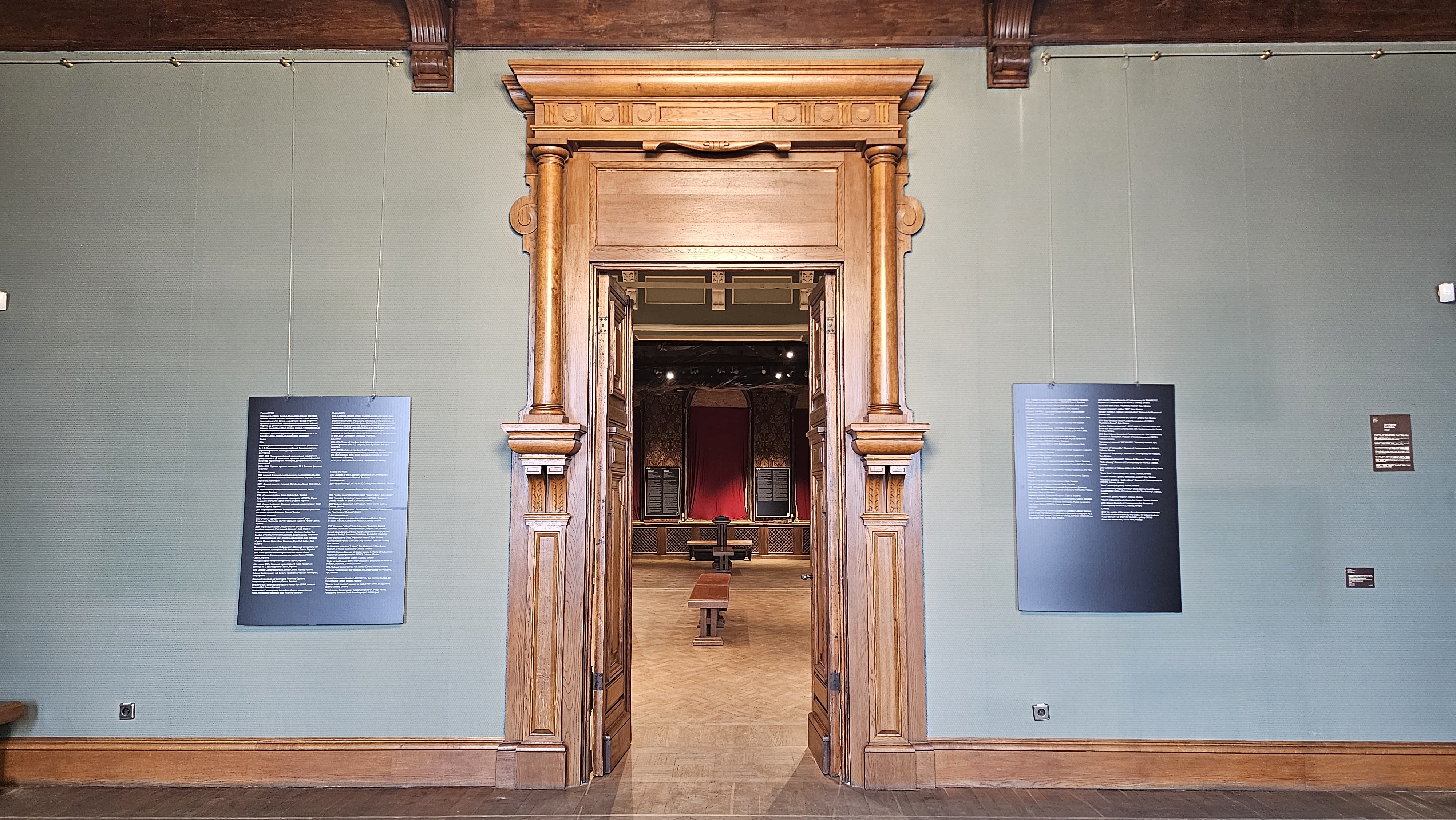 Entrance to an exhibition room of the Khanenko museum. The door frames are of light wood, instead of the paintings of the collection, to presentation boards hang on almond green walls.