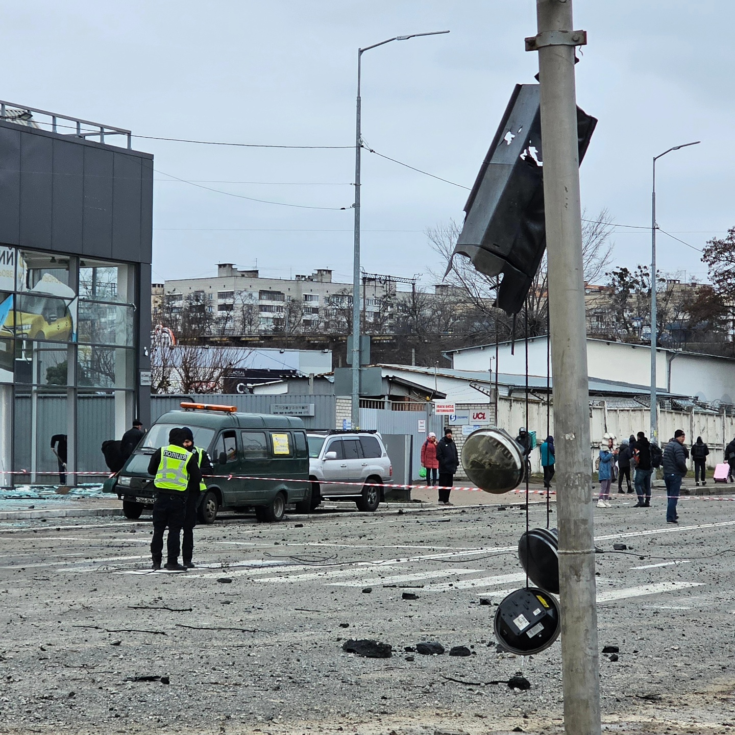 Destroyed traffic lights hang in an industrial site of Podil district, following a missile strike, people are looking on, emergency workers are seen behind a cordon.