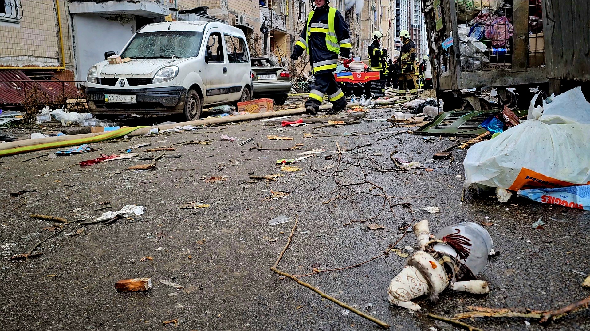 A Christmas snowman decoration among the debris found on the site of a missile strike against a residential building in Kyiv, firefighters walk past, there are debris and shards on the ground.