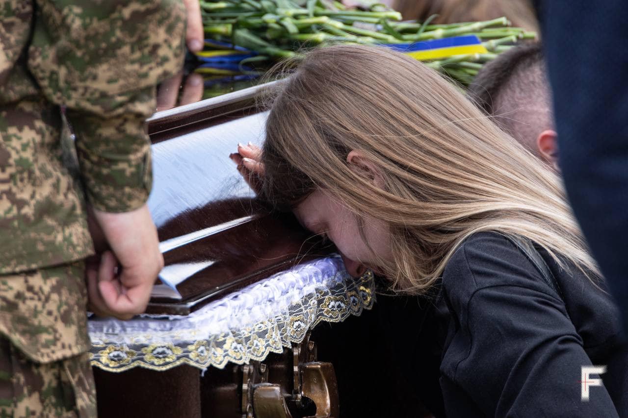 A woman kneels in front of the casket of Denys Zeleniy at his funeral © Danylo Dubchak for Frontliner