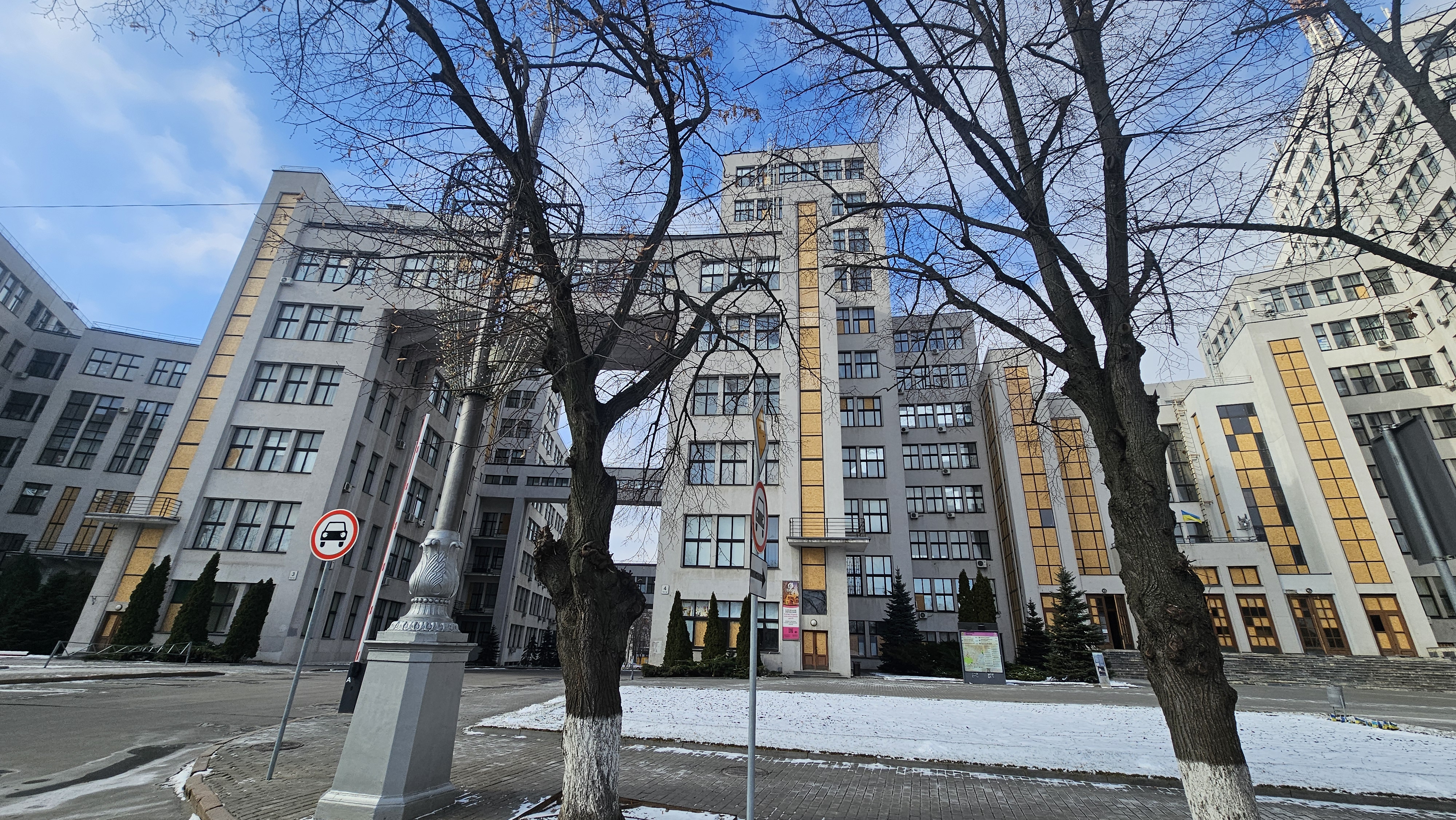 Derzhprom building as seen on February 8th, 2025. Many windows are covered with wooden panels due to russian strikes. Wintry but sunny weather.